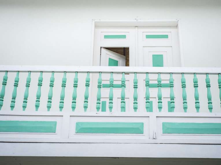 Le balcon d'une maison blanche aux balustrades vertes.